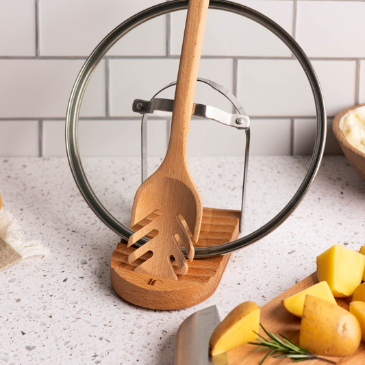 Wooden spoon and spatula set on a wooden stand with a kitchen counter and potatoes in the background.