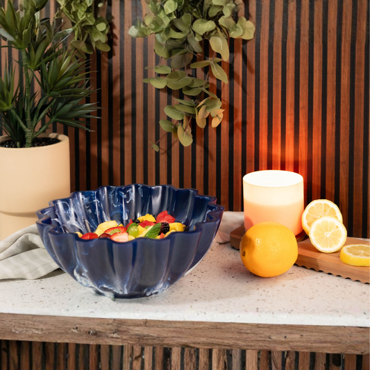 Blue decorative bowl with fruit on a table next to a candle and lemons.