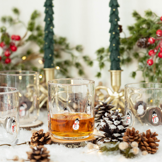 Glass with amber liquid on a festive table setting with pine cones and candles.