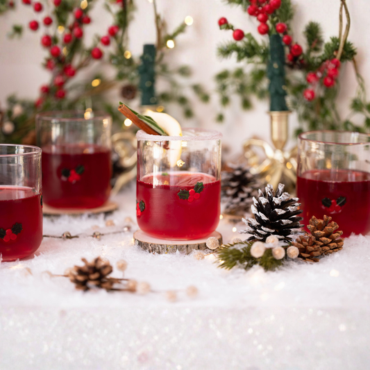 Red cocktails with garnishes on a snowy surface with Christmas decorations.