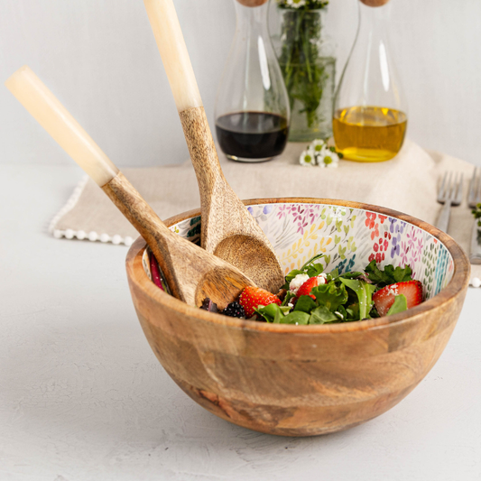 Wooden salad bowl with salad and wooden spoons on a light surface.