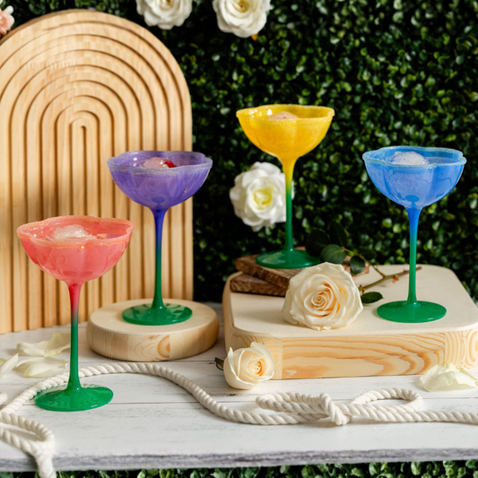 Colorful cocktail glasses on a wooden stand with flowers and a decorative arch in the background.