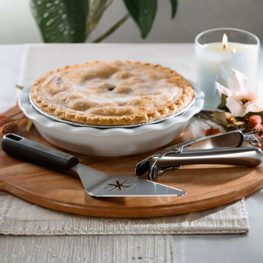Apple pie on a wooden cutting board with a pie server and a lit candle in the background.