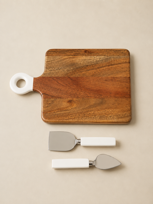 A rectangular wooden serving board with rounded corners and a white loop handle, shown with two matching white-handled metal serving utensils on a warm beige background.