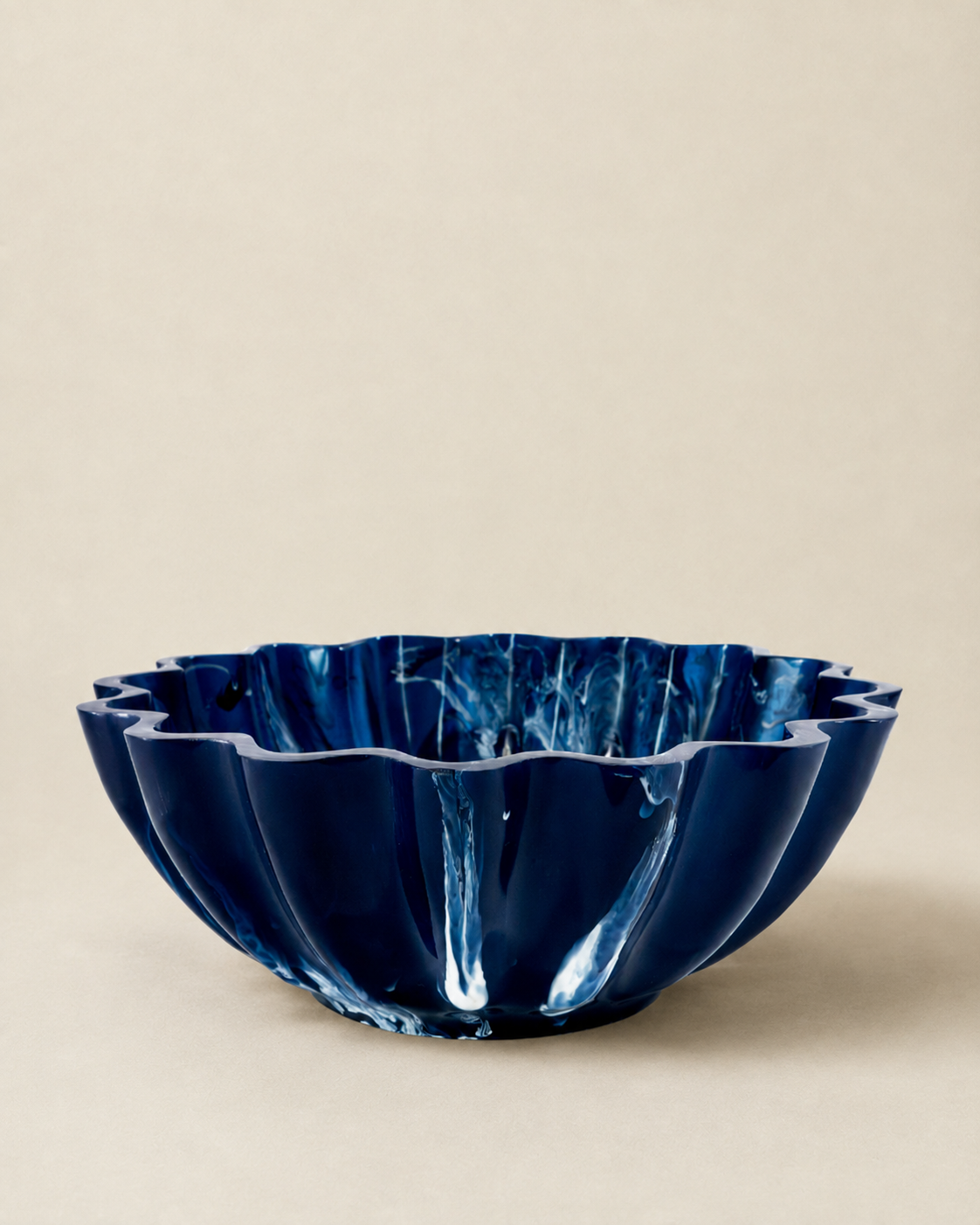 A deep cobalt blue glass bowl with a scalloped, fluted rim, shown on a neutral beige background.