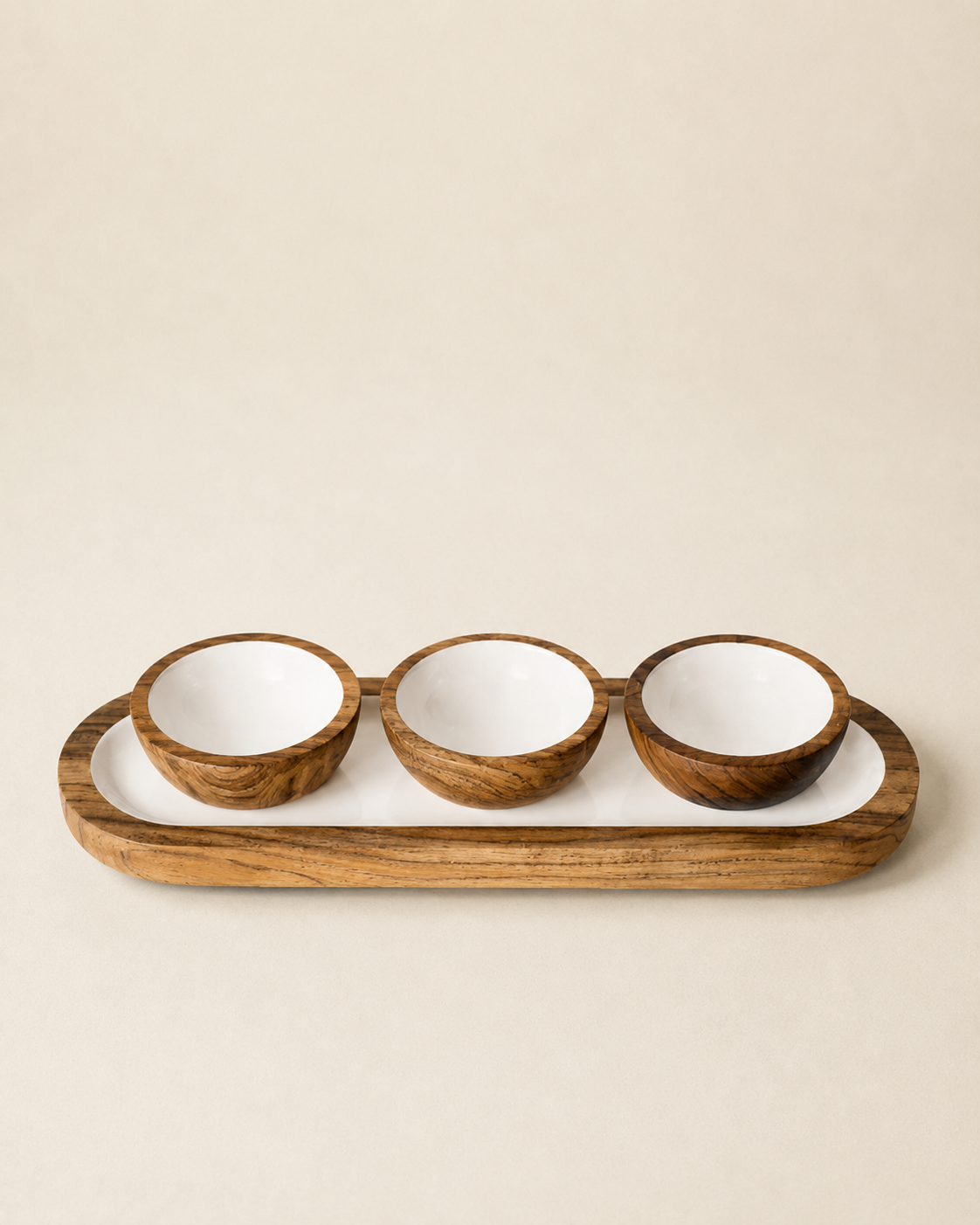 Three small wooden bowls with white interiors arranged in a row on a matching wooden tray with a white base, photographed against a plain warm beige background.