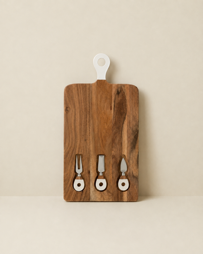 A rectangular wooden serving board with a white hanging loop at the top and three small metal serving utensils mounted along the bottom, shown against a plain warm beige background.