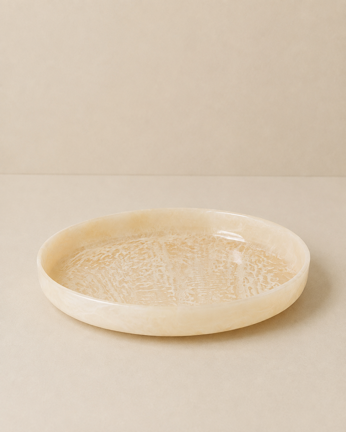 A shallow round tray made of cream-colored bone or shell with a textured, crackled interior, set against a matching beige background.