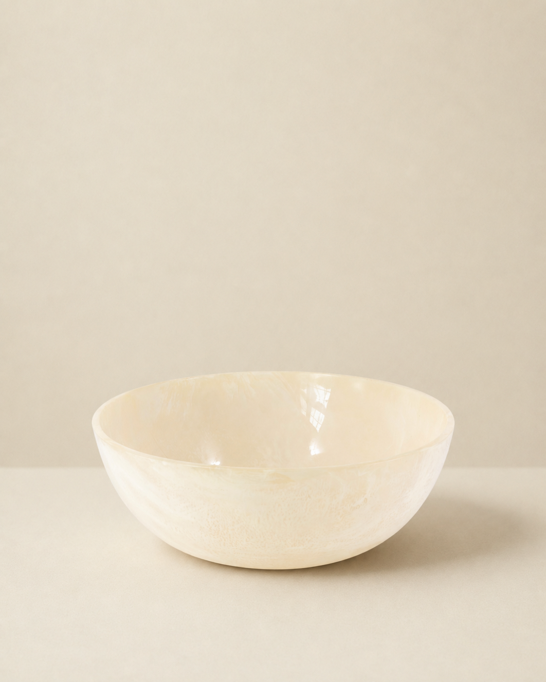 A shallow, wide ceramic bowl with a textured, hand-painted finish in a warm cream or off-white color, set against a minimalist beige background.
