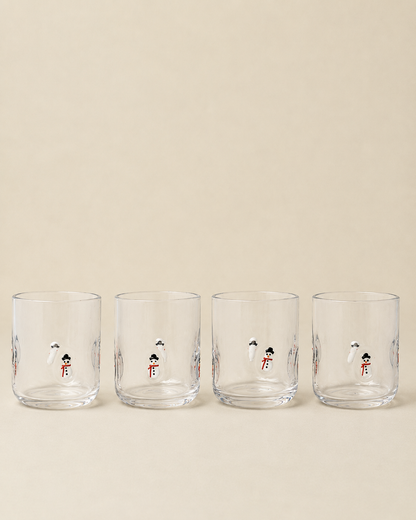 Four clear glass tumblers with small illustrated snowman designs, arranged in a row against a warm beige background.