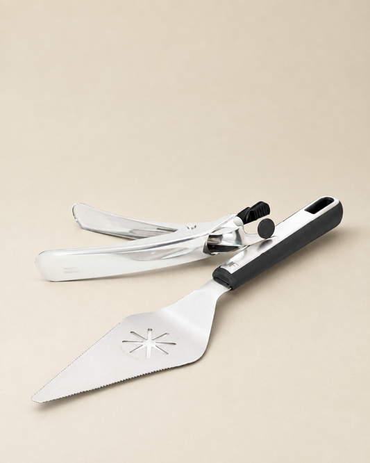 A stainless steel cake server and spatula set with a black handle, displayed on a solid beige background.