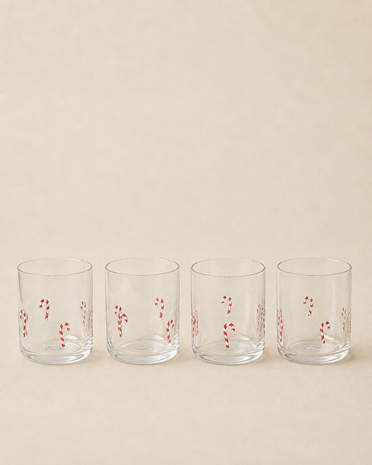 Four clear lowball glasses with red and white candy cane patterns, lined up in a row against a solid beige background.