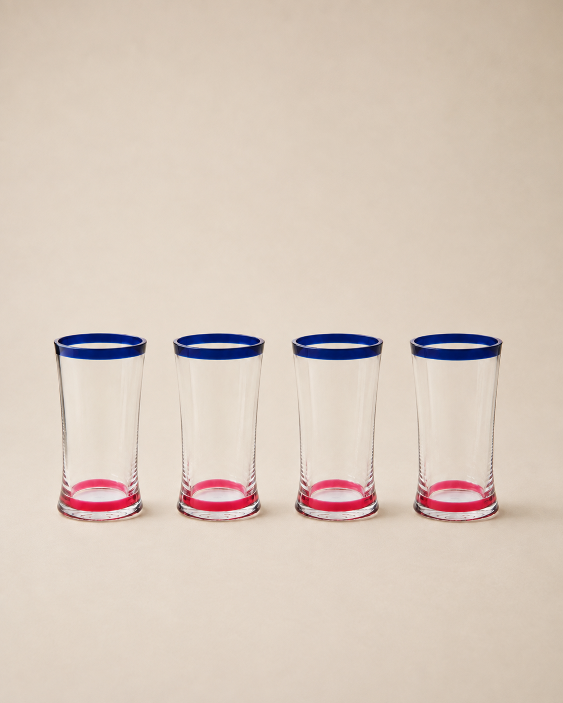 Four clear shot glasses lined up in a row, each featuring a vibrant blue rim and a pink base, set against a solid beige background.