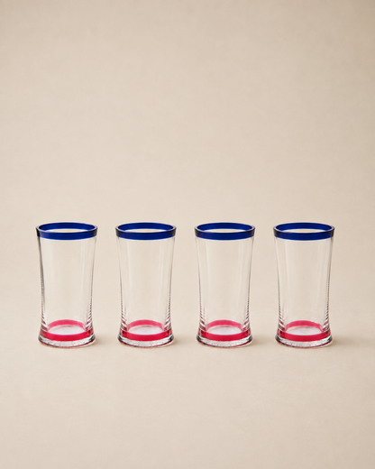 Four clear shot glasses lined up in a row, each featuring a vibrant blue rim and a pink base, set against a solid beige background.
