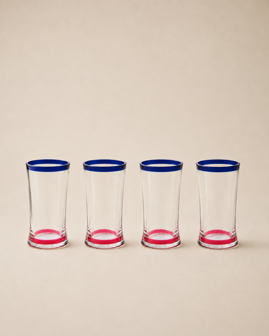 Four clear shot glasses lined up in a row, each featuring a vibrant blue rim and a pink base, set against a solid beige background.